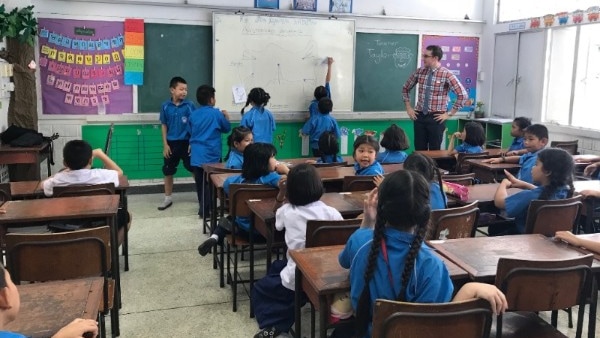 Taylor Weule in Thai primary school classroom with students drawing on board and sitting at desks