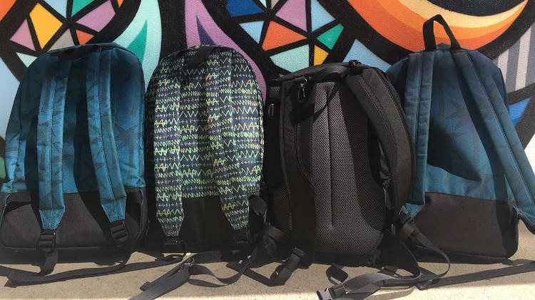 4 school backpacks lined up against wall 