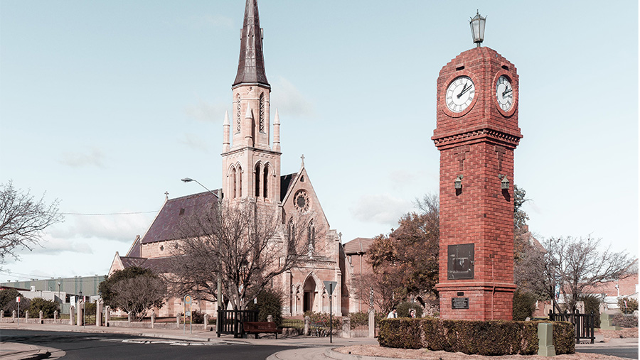 The main street of Mudgee NSW, featuring a red brick clocktower next to a Gothic style church.
