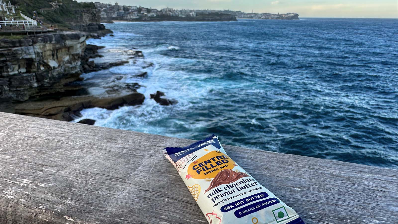 A Stroom protein bar is sitting on a wooden fence overlooking a beachside cliff