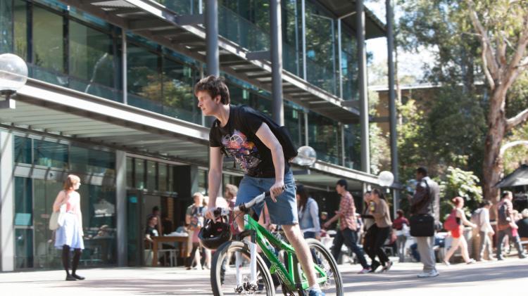 Student riding bike on Wollongong campus outside Library