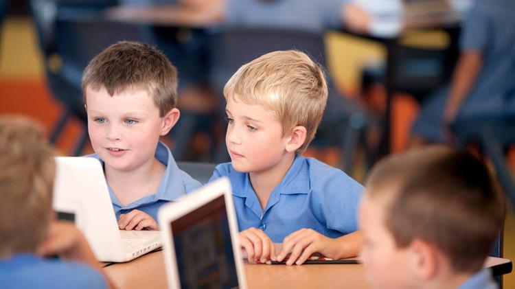 Two primary school boys play on tablets in a classroom