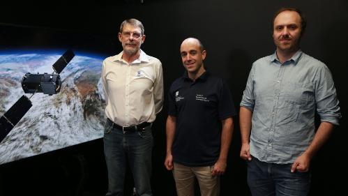 Associate Professor Andrew Zammit Mangion, Distinguished Professor Noel Cressie and Dr Michael Bertolacci standing in front of a screen showing a satellite over Earth