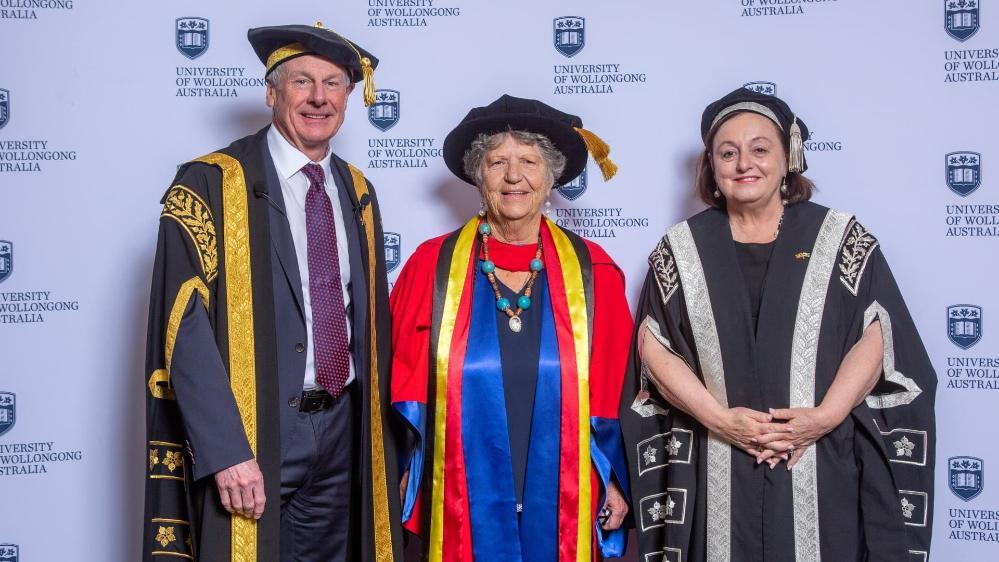 UOW Deputy Chancellor Robert Ryan, Dr Aunty Joyce Donovan, and UOW Vice-Chancellor Professor Patricia Davidson stand together in front of a UOW wall. Photo: Andy Zakeli