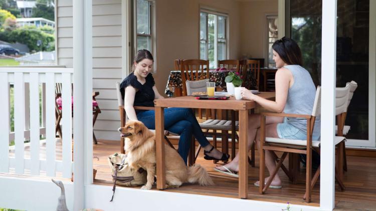 two females sitting at an outdoor table with a dog beside them