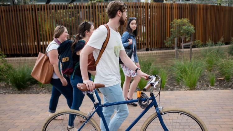 Student pushing bike along path with other students
