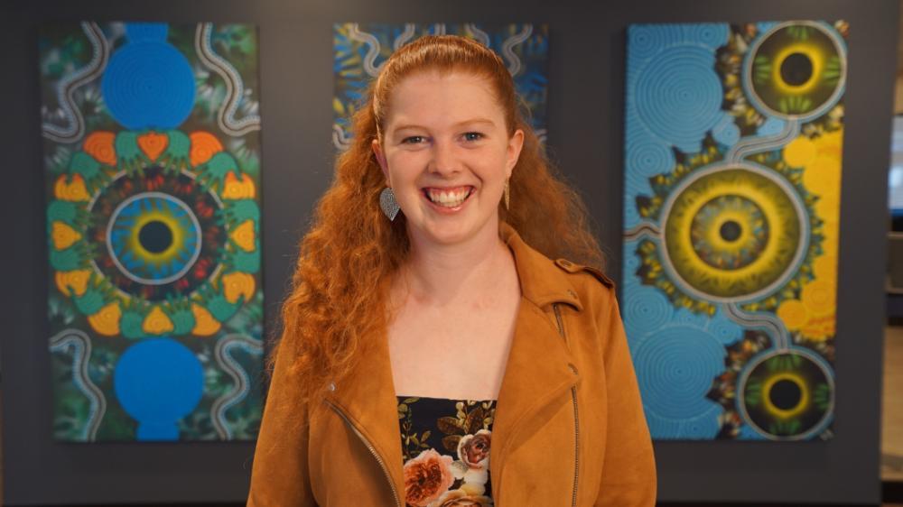 Meg Cummins smiling in front of Aboriginal artwork