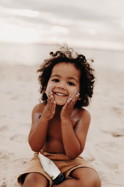 A child rubbing skincare onto their face at the beach