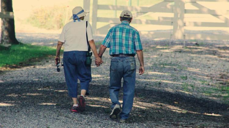 An elderly couple holds hands walking down a country lane