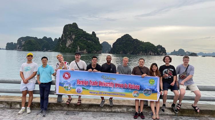 Associate Professor Thanh Le and Associate Professor Amir Arjomandi are holding a large long blue banner  with UOW Business School  in front of river in Vietnam.