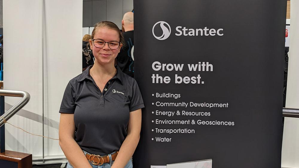 Jessica Don stands infront of her employers marketing banner, Stantec