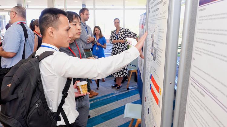 Attendees browsing presentations on whilebroads at the 2023 Inaugural Rural Health Conference. A man stands in the foreground wearing a white shirt pointing to the display.