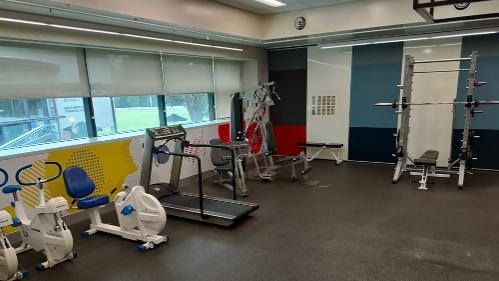 Exercise bikes, treadmills and other excise equipment placed in area with windows and a grey floor.