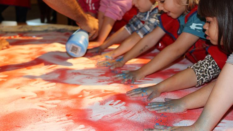 Preschool aged children creating an indigenous inspired poster with their handprints