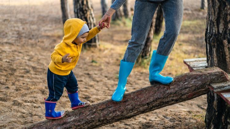 Photo of Child and Adult walking on log with gum boots