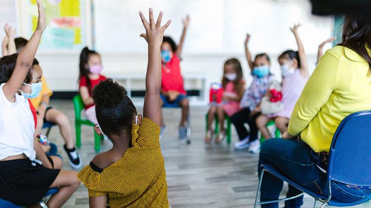 Early Educator sitting with Children who have their hands raised, in a relaxed setting