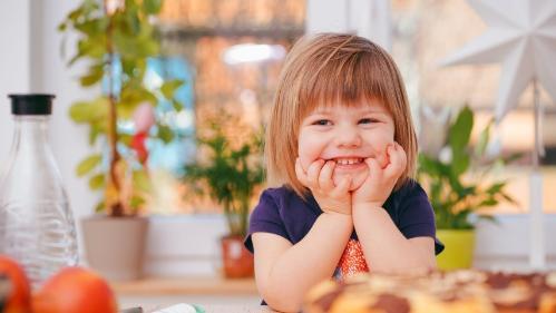 3 year old girl sitting at table, smiling with her chin resting on the hands