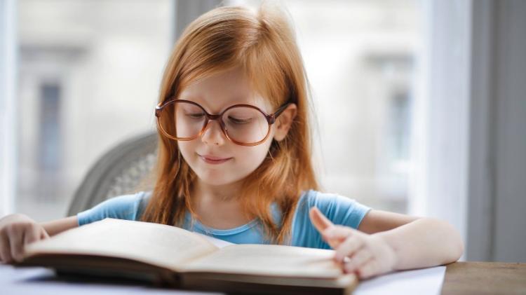 Girl with long ginger hair reading a book, wearing glasses