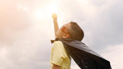 Young boy with cape on, fist bumping the sky