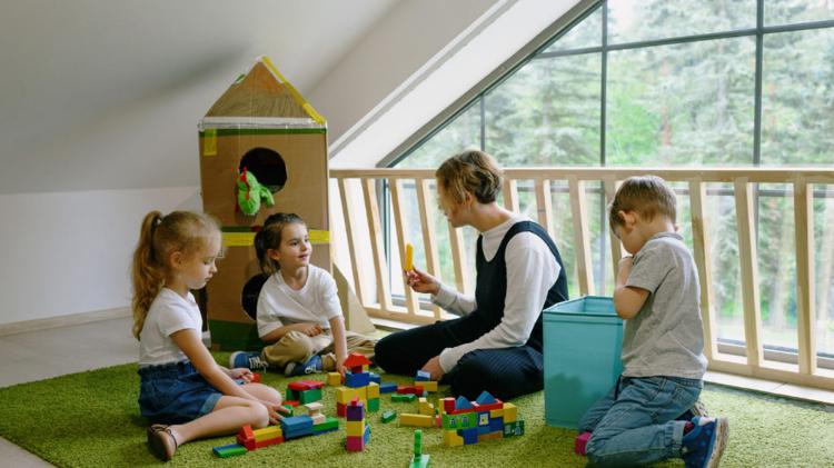 Female educators plays with toys on a mat with 4 preschool children