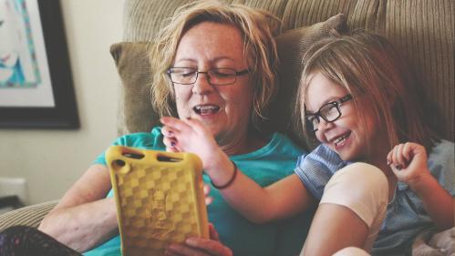 Photo of Nanny and Granddaughter sitting on couch using a tablet computer