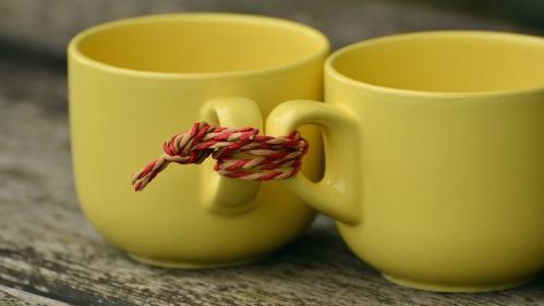 Two yellow mugs sitting on a table, tied together with string
