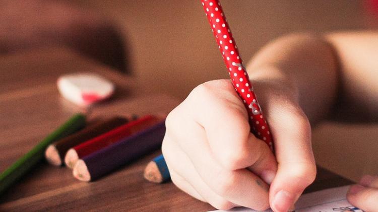 Child drawing with a red pencil on a piece of paper