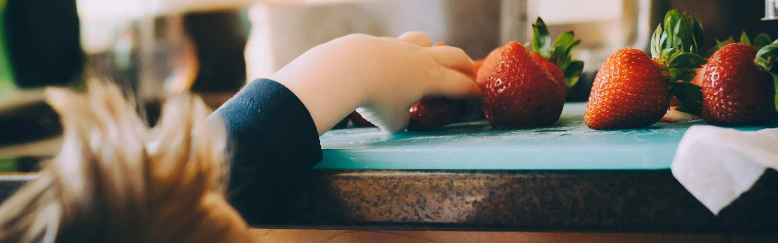 Child reaches for strawberries on kitchen counter