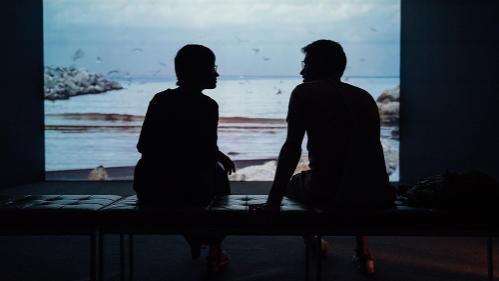 Two people sitting looking through window to ocean