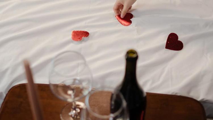 Someone laying hearts on a bed with Champagne in foreground