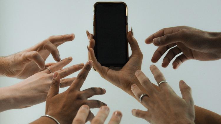 one hand holding a phone with 6 hands reaching for phone