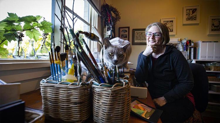 Photo of Gai Lindsay sitting in her art studio with her cat looking at the camera