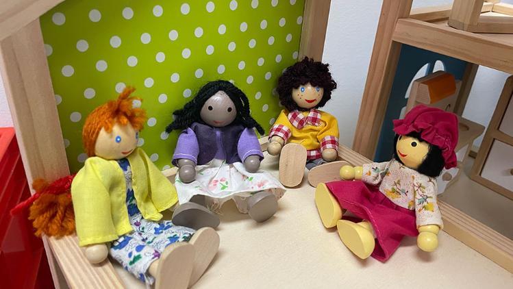 5 kids dolls sitting on table dressed in a varety of clothing