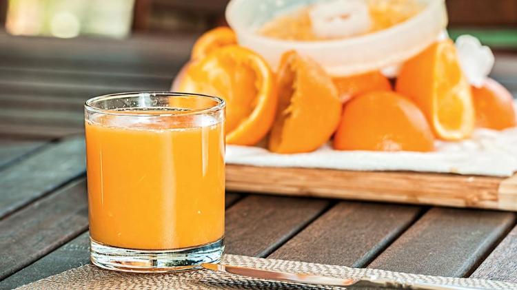 Glass of Orange Juice on table with squeezed oranges in background