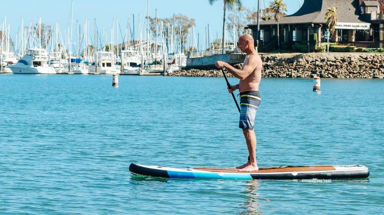 Bald man in boardshorts paddling on Stand Up Paddleboard in harbour