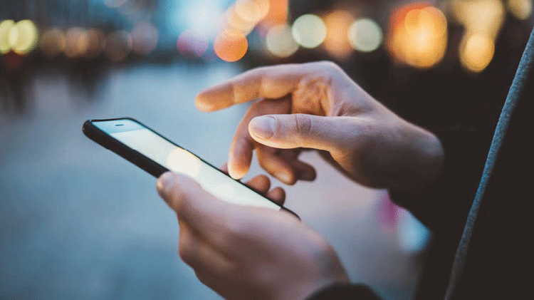 Image of hands holding and using a mobile phone on the street in the evening
