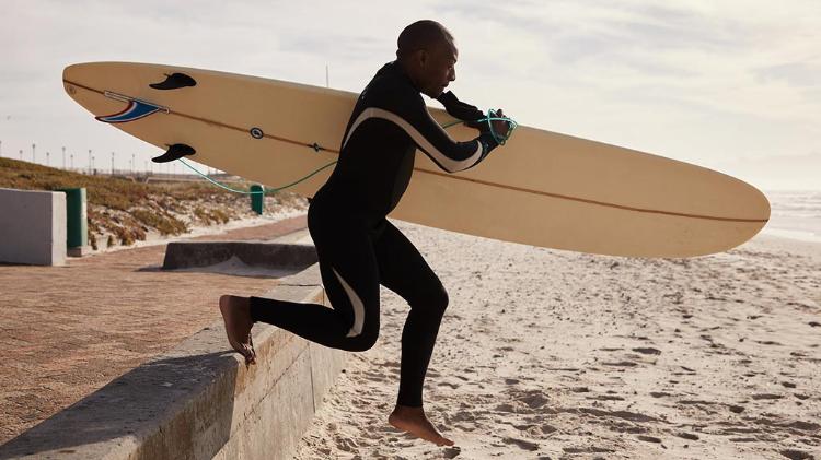 Man in wetsuit with surfboard under his arm, going into surf