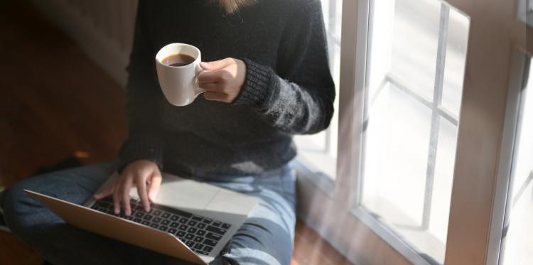 Woman using laptop while holding a cup of coffee