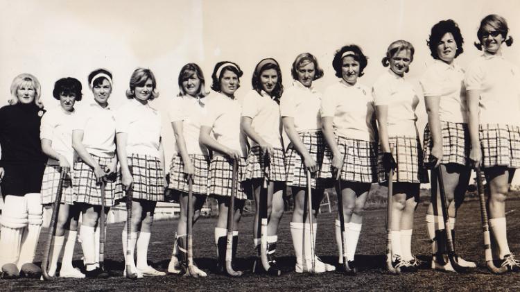 A black and white of young women standing in a line holding hockey sticks