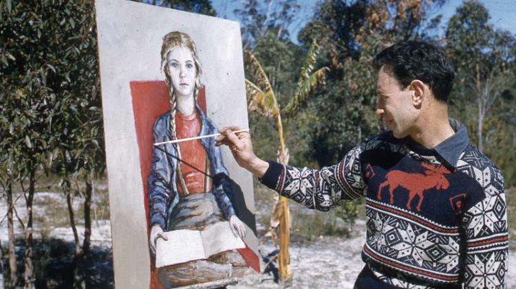 Young Bert Flugelman painting a portrait of a girl while standing in bushland