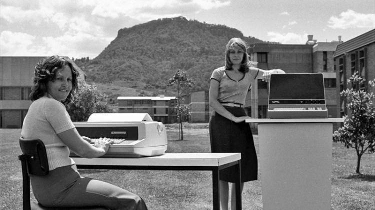 Black and white of two female librarians with vintage computers and Mount Keira in the background