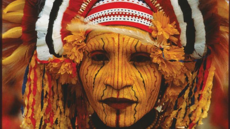 An indigenous woman from Papua New Guinea, covered in orange paint, wearing a bright headdress
