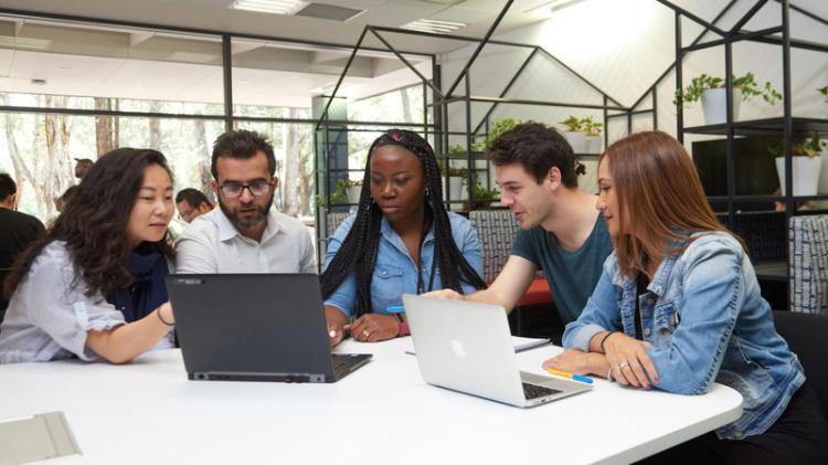 A group of students crowded around some laptops in the informal learning spaces at the Wollongong Campus Library