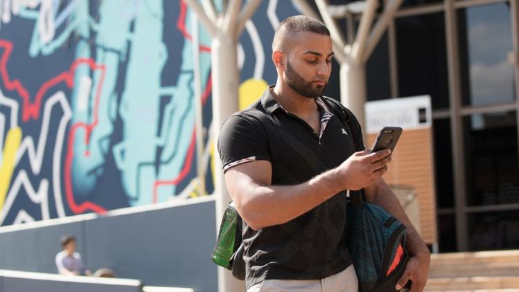 Student standing outside Liverpool campus library holding a mobile phone