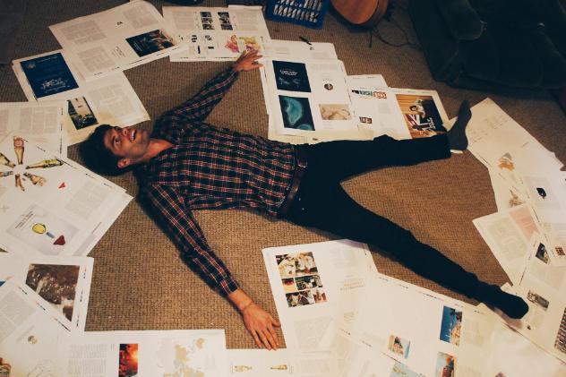 Nicholas laying on the floor surrounded by pieces of paper with album art