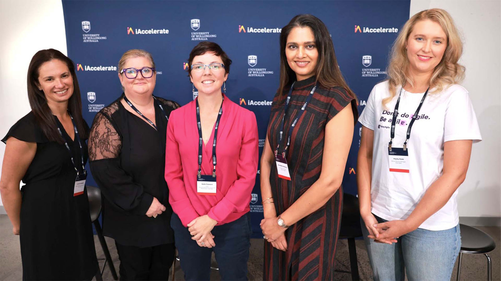 A group of five women are standing in front of a UOW and iAcclerate media wall