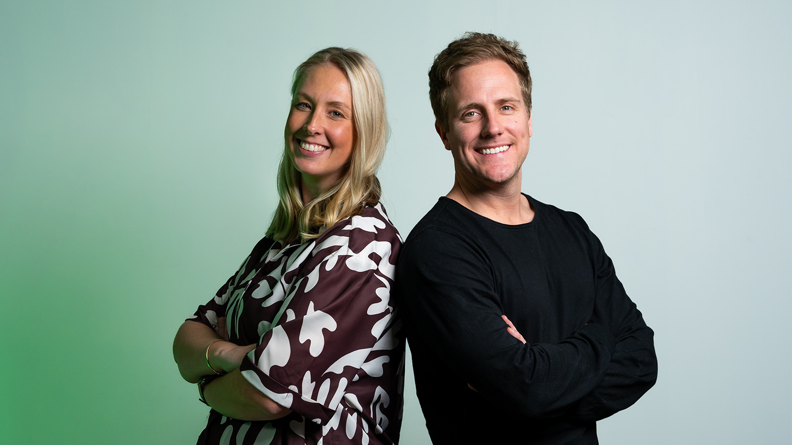 Cassandra Wilkins and Reece Carter are standing back-to-back in front of a green backdrop.