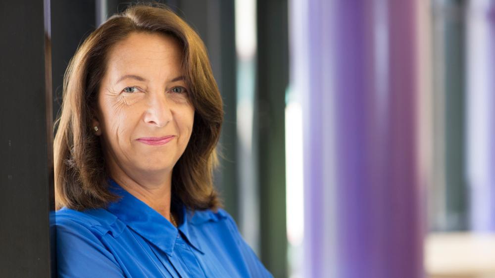 Professor Lorna Moxham smiles while leaning against a wall wearing a blue shirt.