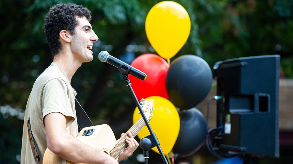 A singer stands on stage with black, yellow and red balloons behind him. Photo: Paul Jones