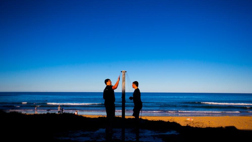 Two people stand under a shower at the beach, against a blue sky. Photo: Paul Jones